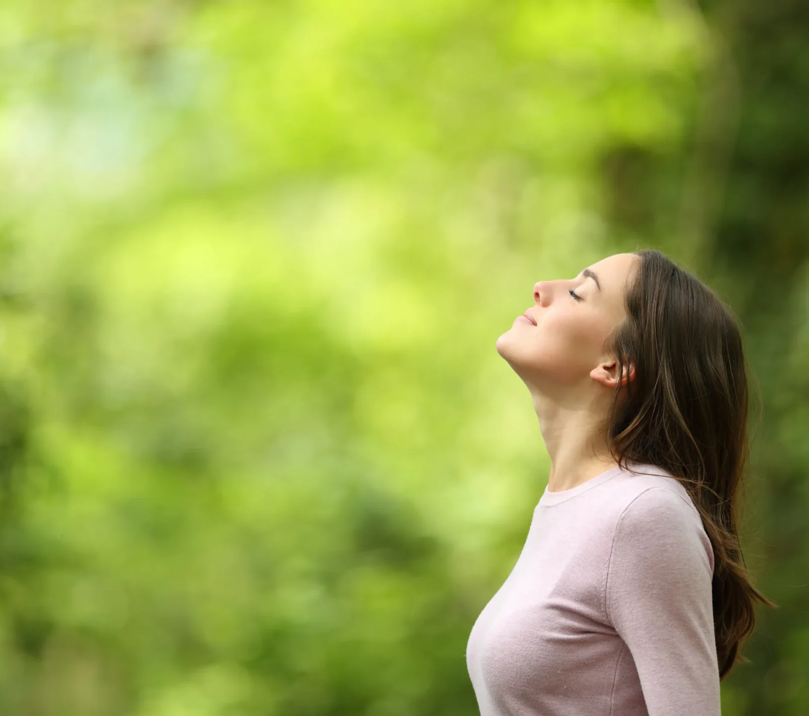 Women standing outside in a forest with her eyes closed and taking a deep breath